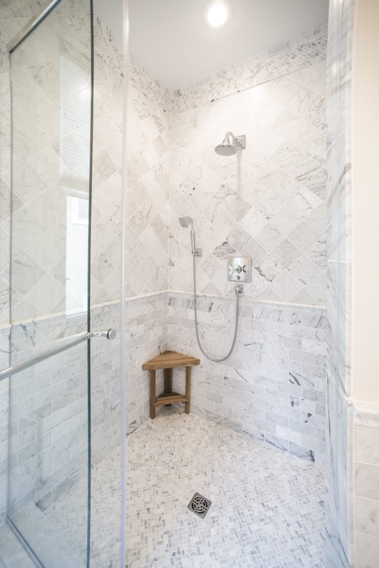 large bright shower stall with glass door and marble tiling