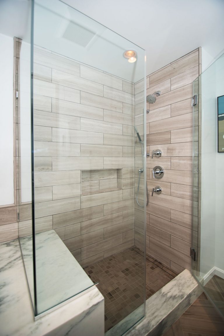 large shower stall with built in bench and glass door storage nook