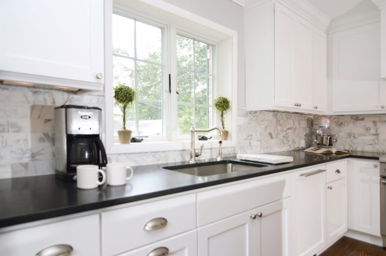 bright white cabinetry and large window over sink dark countertops and tile backsplash