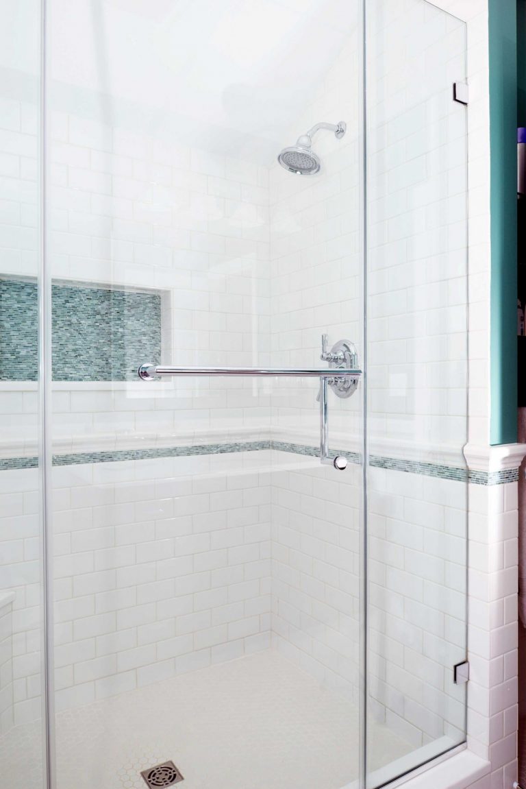 shower stall with glass door and built in storage nook with teal mosaic tile feature
