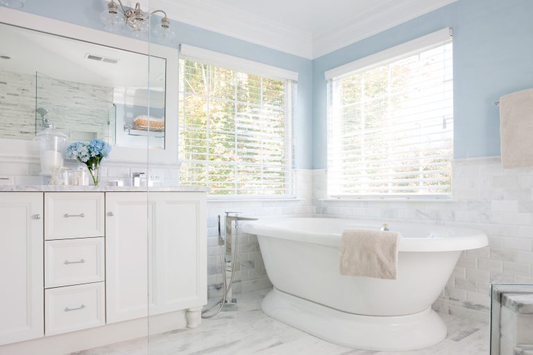 farmhouse style white and blue bathroom with large windows over freestanding tub