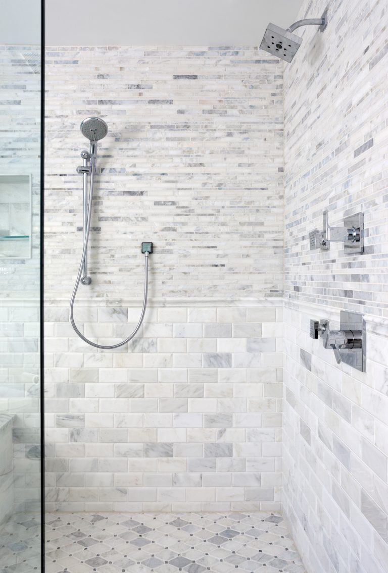 large shower with multiple showerheads built in storage nooks and marble tile