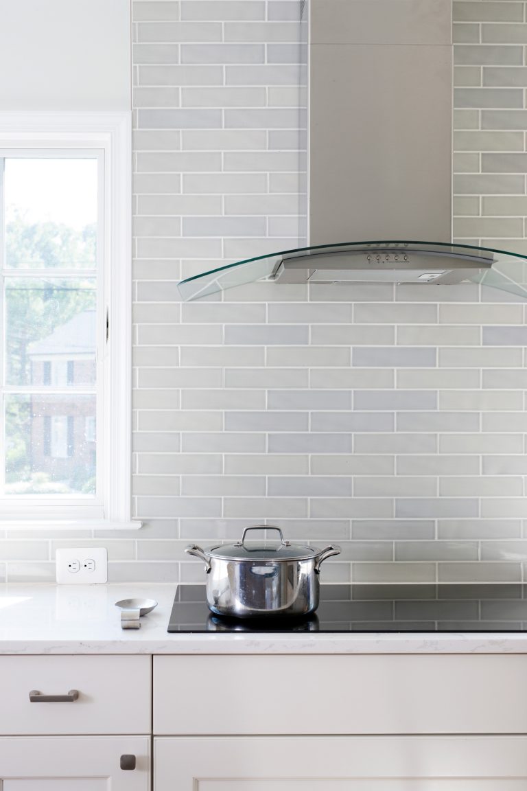 electric stovetop with glass and stainless steel hood white cabinetry mixed tone gray subway tile backsplash to ceiling