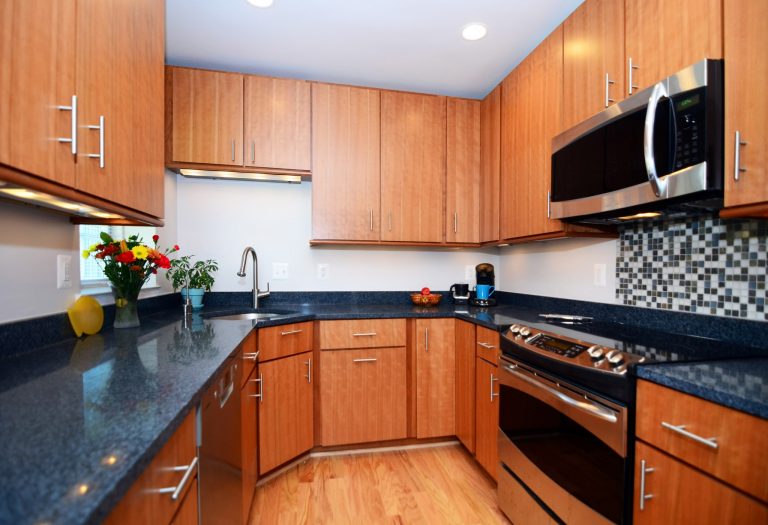 sleek modern DC kitchen with medium stain wood floors and cabinetry and dark countertops mosaic tile backsplash stainless steel appliances recessed and under cabinet lighting