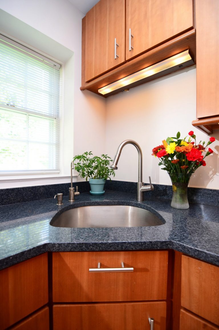 sleek modern DC kitchen with medium stain wood cabinetry and dark countertops stainless steel sink under cabinet lighting