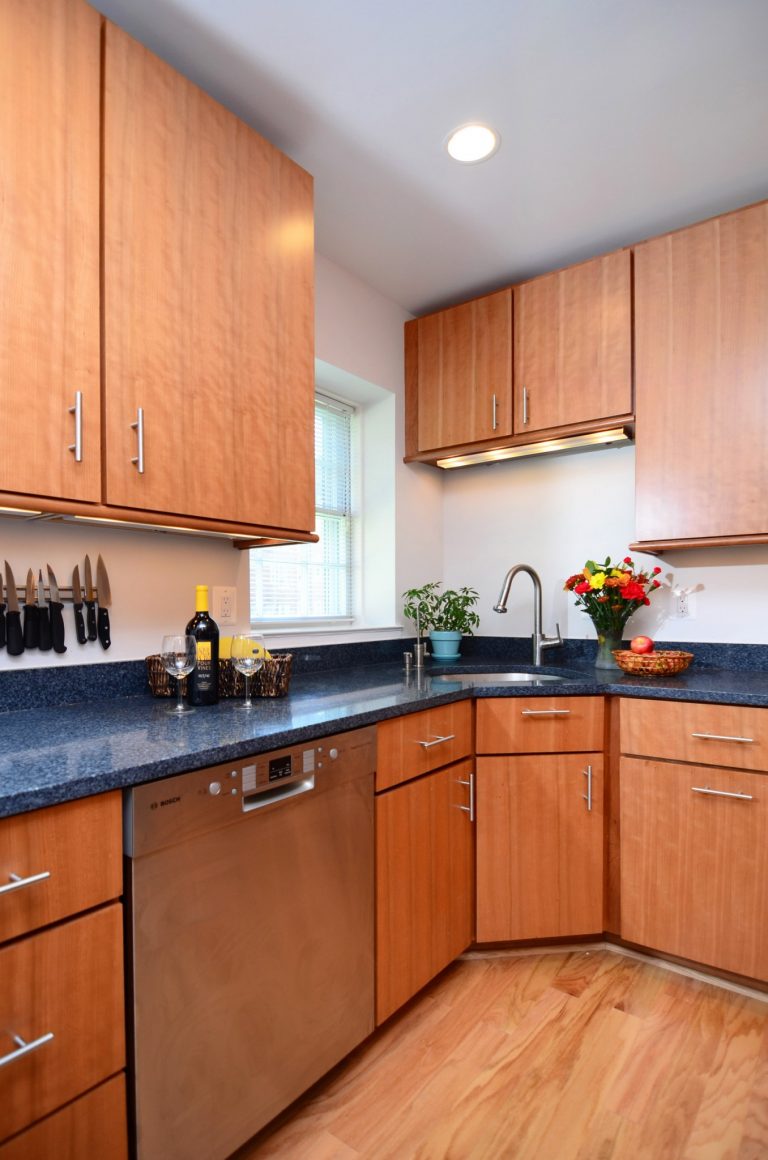 sleek modern DC kitchen with medium stain wood floors and cabinetry and dark countertops stainless steel appliances and recessed lighting