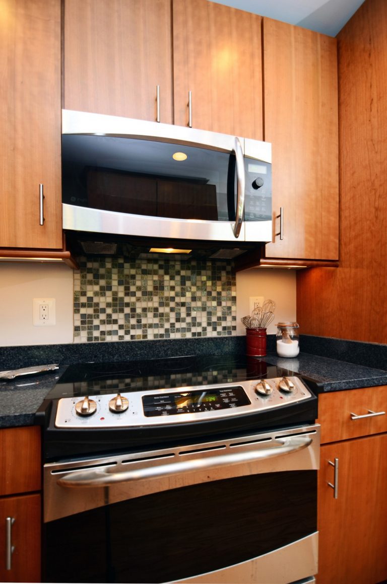 modern kitchen with medium wood cabinetry and cool tone mosaic backsplash detail behind stainless steel electric range