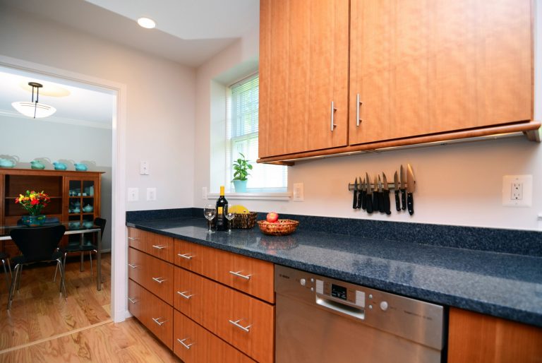 sleek modern DC kitchen with medium stain wood floors and cabinetry and dark countertops stainless steel appliances and recessed lighting