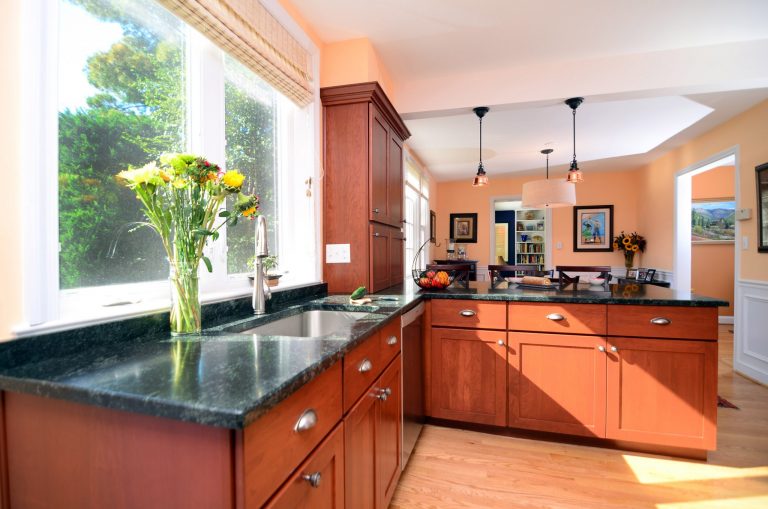 open kitchen medium stain cabinetry dark countertops large windows pendant lighting over peninsula warm color tones