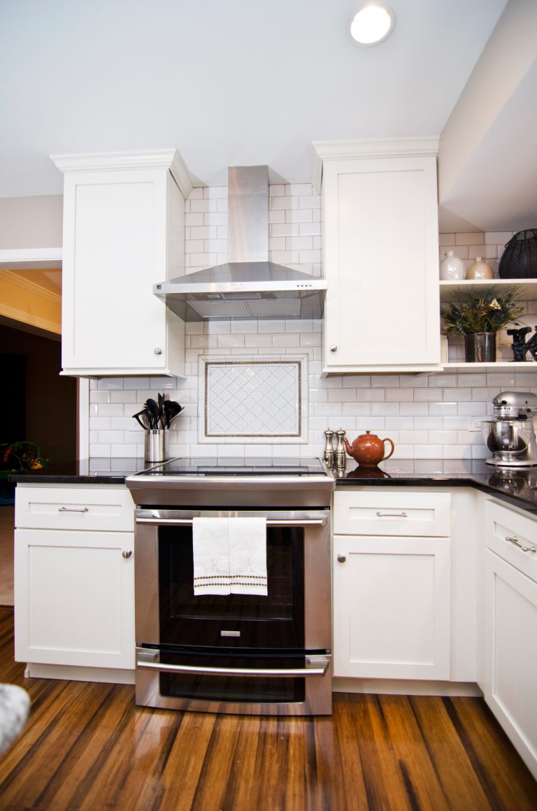 farmhouse style kitchen white cabinetry natural wood floors backsplash detail stainless steel electric range and hood