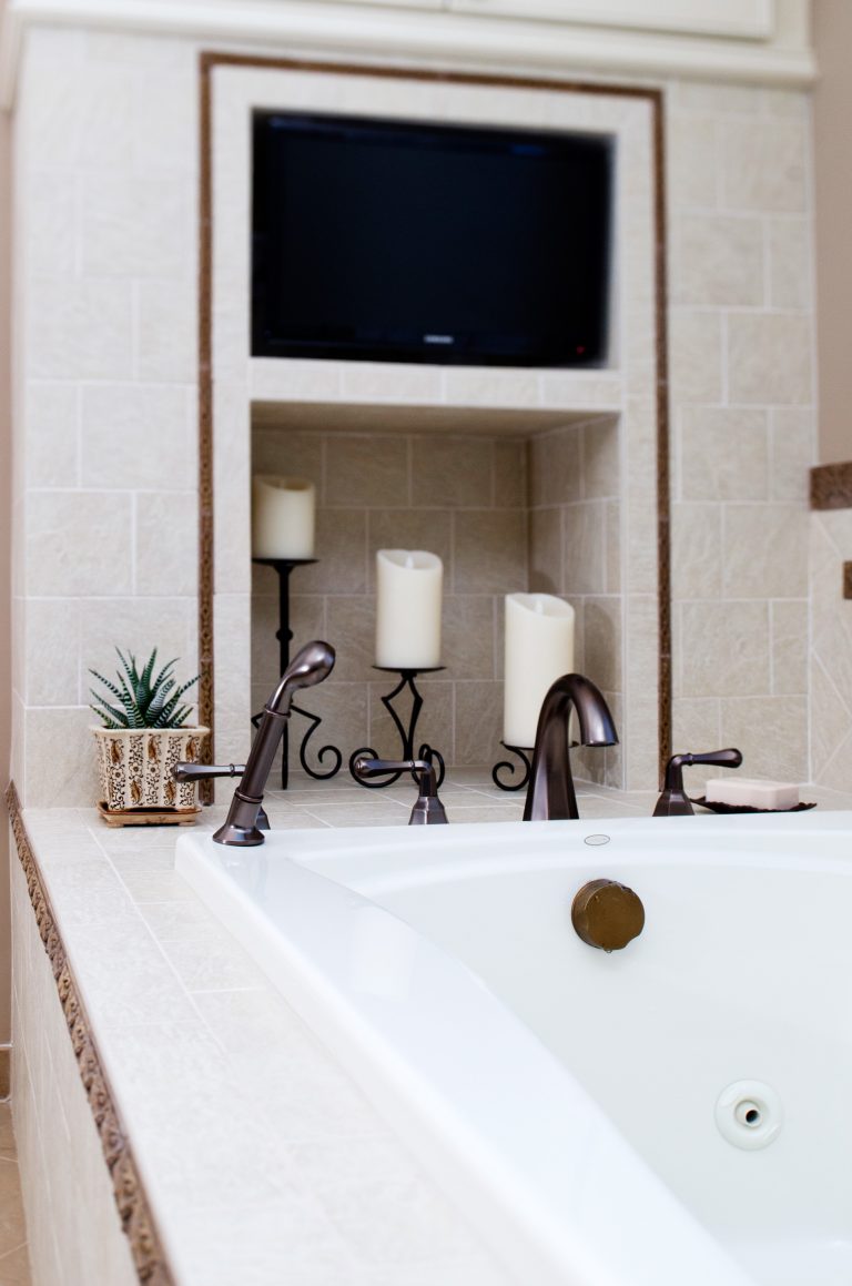 renovated bathroom with tv and storage nook next to tub