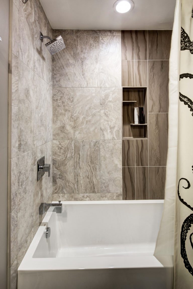 tub and shower combo in modern bathroom recessed lighting and built in storage nook brushed fixtures natural beige color palette mixed texture tiles