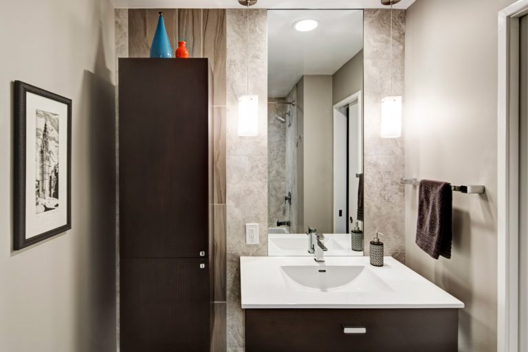 modern bathroom dark wood floor to ceiling cabinetry and vanity sconce lighting neutral beige color palette mixed texture tiling