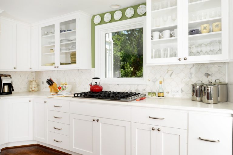 traditional farmhouse style kitchen white cabinetry with glass doors on uppers gas range stovetop in front of window