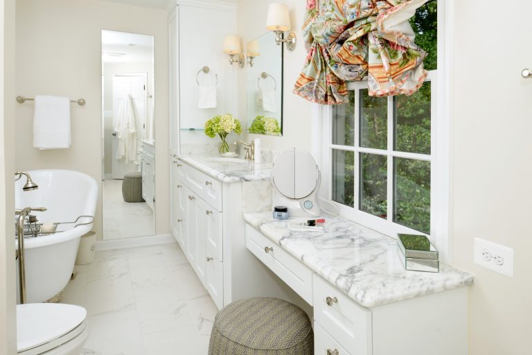 bright white bathroom with marble floors freestanding clawfoot tub with brass hardware marble countertops and makeup area