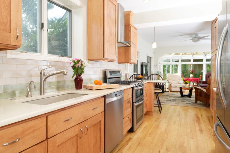 craftsman style kitchen natural stained wood cabinetry with peninsula and neutral color subway tile backsplash stainless steel appliances electric range and glass hood flows into living area