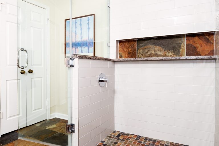 large shower stall with glass door and built in storage nook neutral color palette tile accent