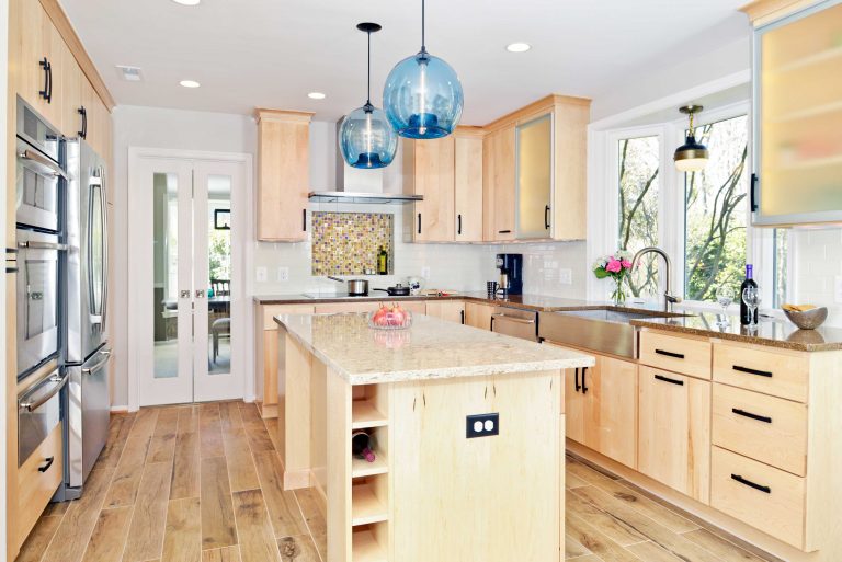 modern kitchen with light wood cabinetry and stainless steel appliances pop of color with blue glass pendant lighting over island