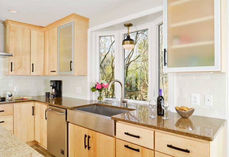light wood cabinetry stainless steel farm sink under bay window upper cabinets with frosted glass doors