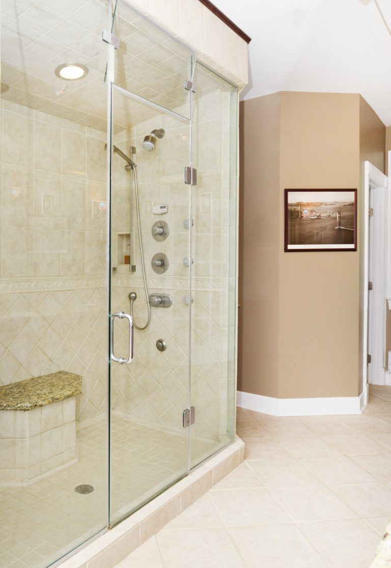 large shower stall with glass door and built in bench tan neutral color palette