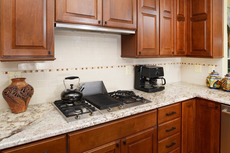 traditional country style kitchen medium stain cabinetry granite countertops gas stovetop backsplash tile detailing