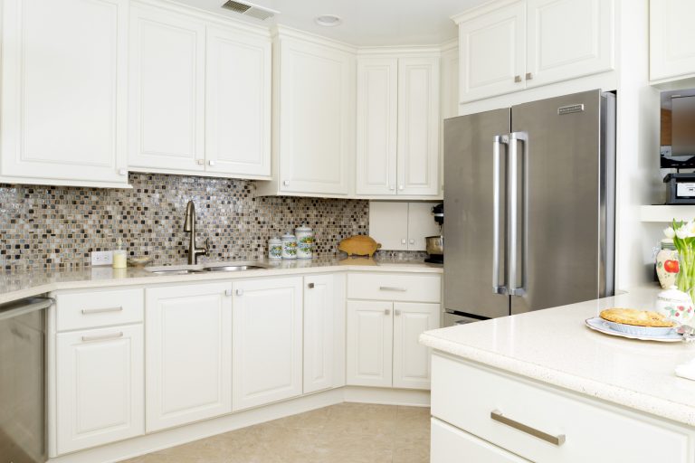 bright white kitchen with peninsula seating mosaic tile backsplash stainless steel appliances gold cabinetry hardware