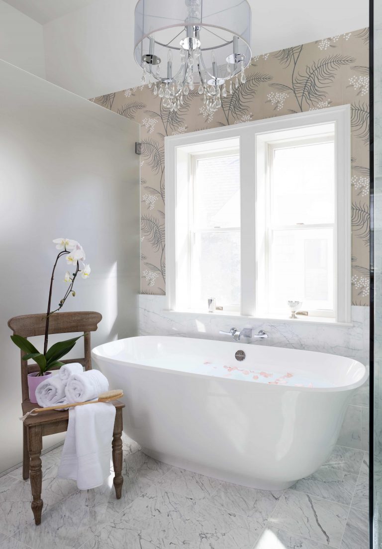 freestanding tub under large window floral wallpaper glass chandelier neutral color palette