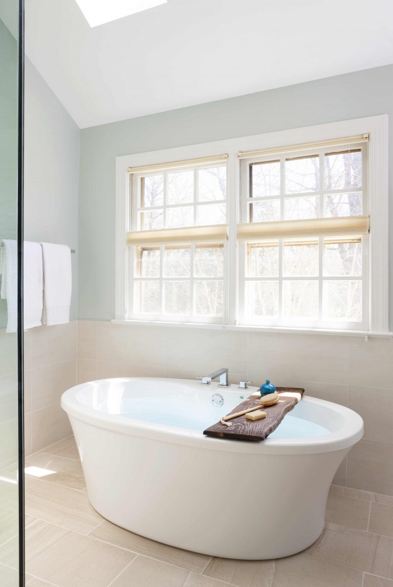 modern double-ended freestanding tub below window and skylight neutral color palette