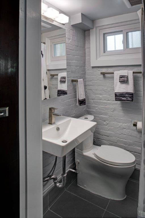 modern industrial style bathroom exposed brick walls painted gray sconce lighting sink with exposed pipes toilet with push button flush