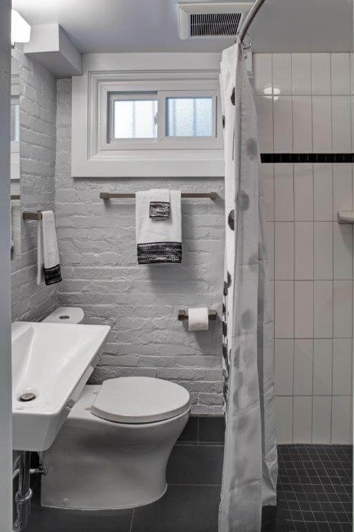 modern industrial style bathroom exposed brick walls painted gray sconce lighting sink with exposed pipes shower with black and white tile