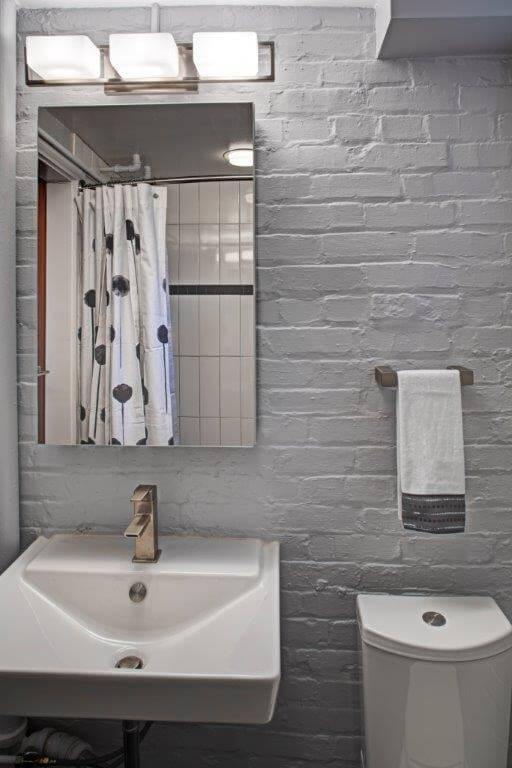 modern industrial style bathroom exposed brick walls painted gray sconce lighting toilet with push button flush