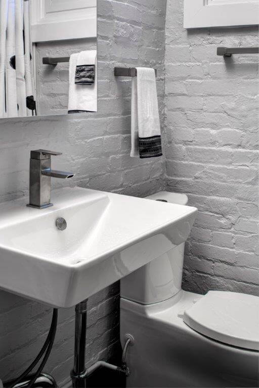 modern industrial style bathroom exposed brick walls painted gray sconce lighting sink with exposed pipes toilet with push button flush