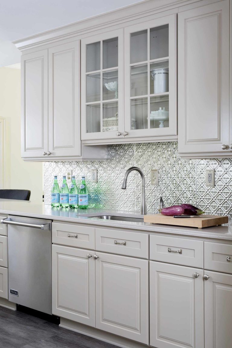 traditional kitchen with cream cabinetry and glass doors on uppers stainless steel backsplash and appliances gray floor