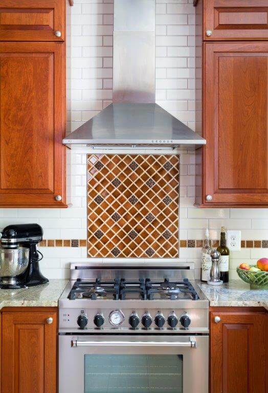 cherry cabinets white countertops stainless steel gas range and range hood tile backsplash detail