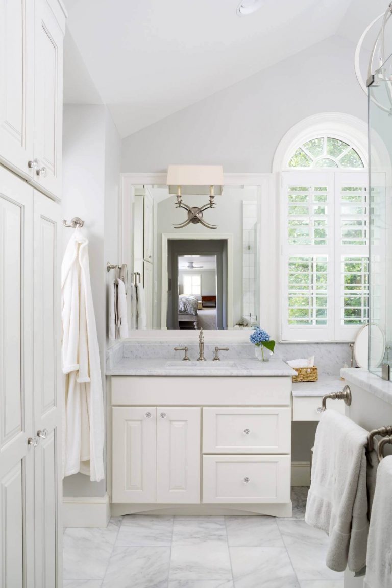 bright white master bathroom with floor to ceiling storage double sinks and built in vanity high ceiling and large window