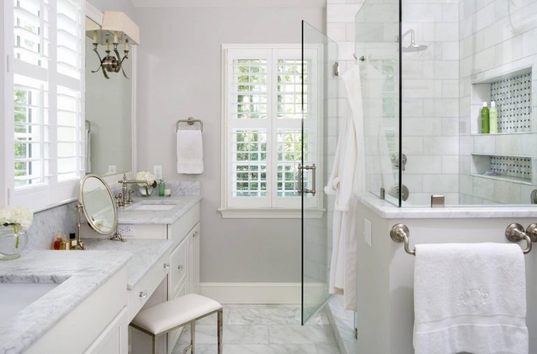 bright white and elegant bathroom double sinks and built in vanity separate shower stall with glass door and built in storage nook gray walls sconce lighting marble floors