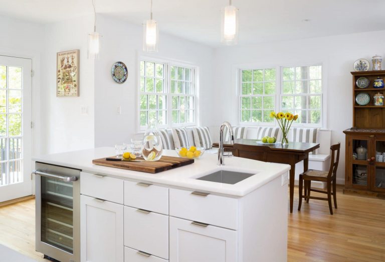 eat in kitchen area island with beverage refrigerator and sink white cabinetry natural wood floors large windows and glass door pendant lighting