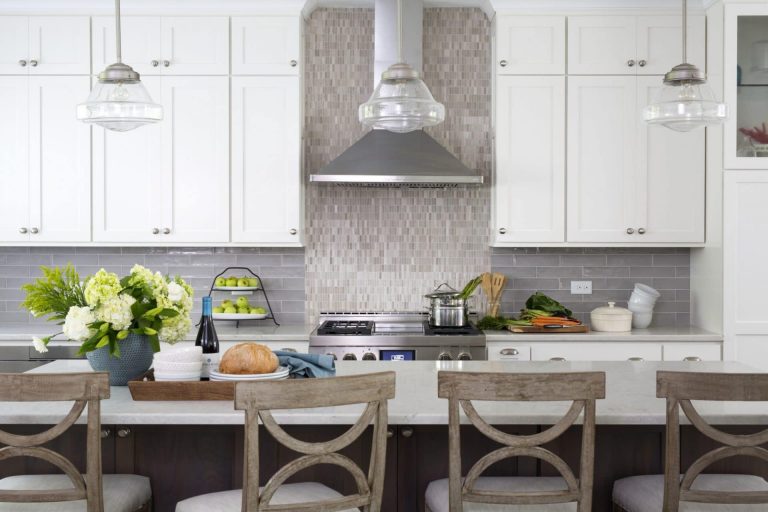 kitchen with neutral and gray color palette white upper cabinets center island with seating and pendant lighting above tile backsplash with feature tile to ceiling behind range hood