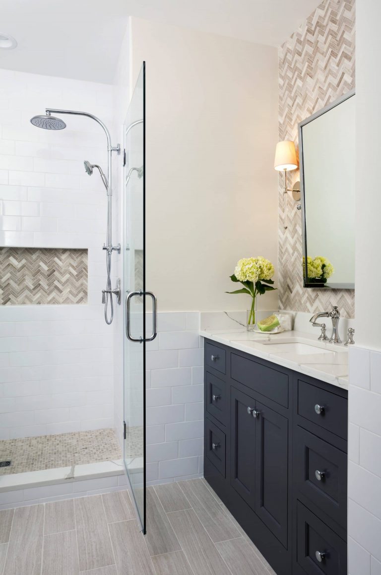 vanity with navy blue cabinetry accent tile behind mirror separate shower stall with glass door and accent tile in built in storage nook