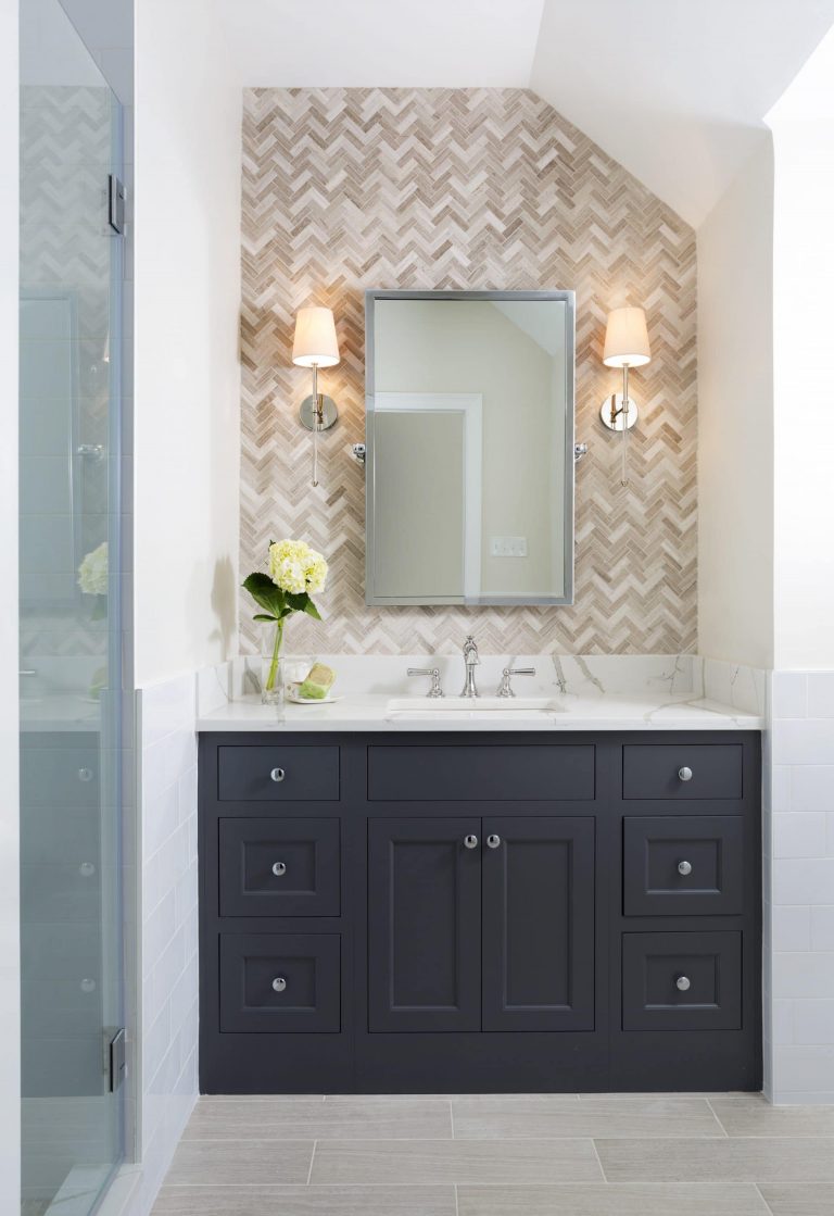 bathroom vanity with navy blue cabinetry white countertop tile feature wall behind mirror sconce lighting