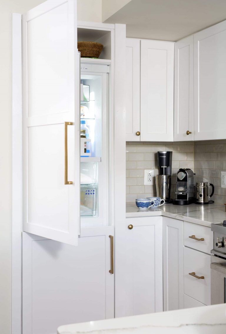 kitchen refrigerator with white cabinetry paneling and gold hardware