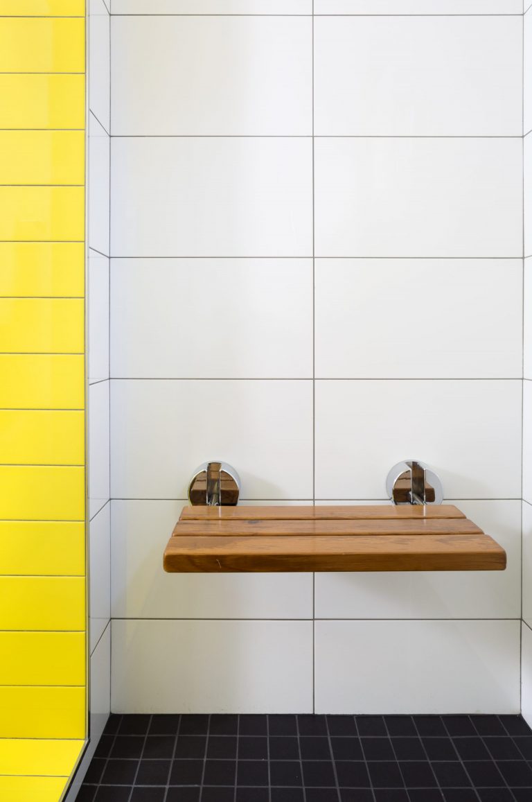 built in wooden shower bench and pop of color yellow tile