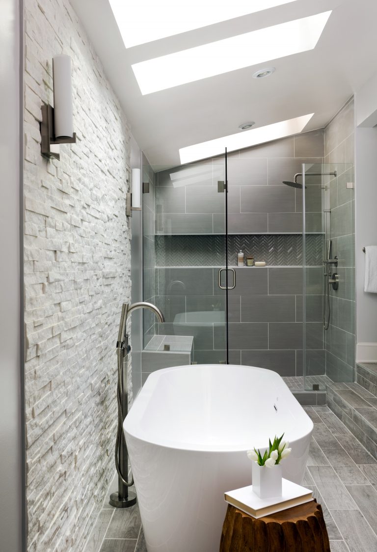 modern bathroom gray color palette separate tub and shower stall with glass door textured stone feature wall skylight