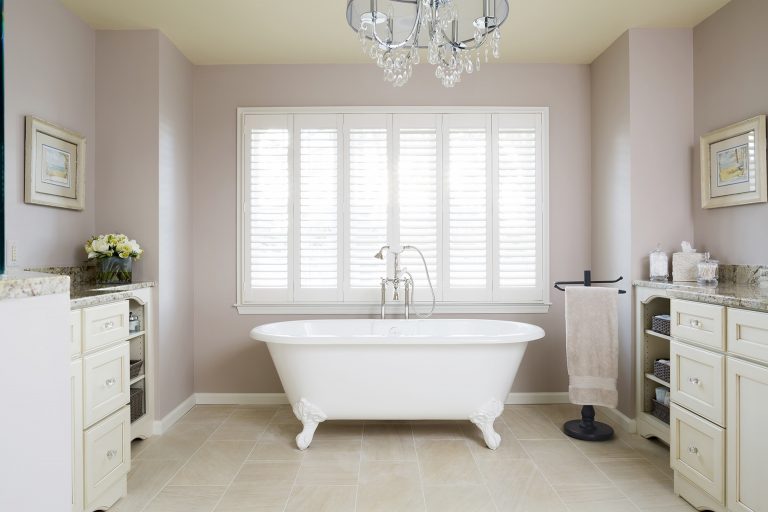 freestanding tub in master bathroom under large window and chandelier two separate vanities with sinks