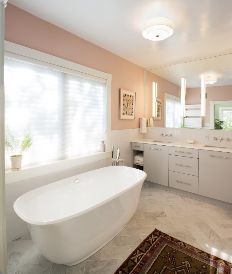 bathroom with neutral pink color palette freestanding tub under window white vanity cabinetry