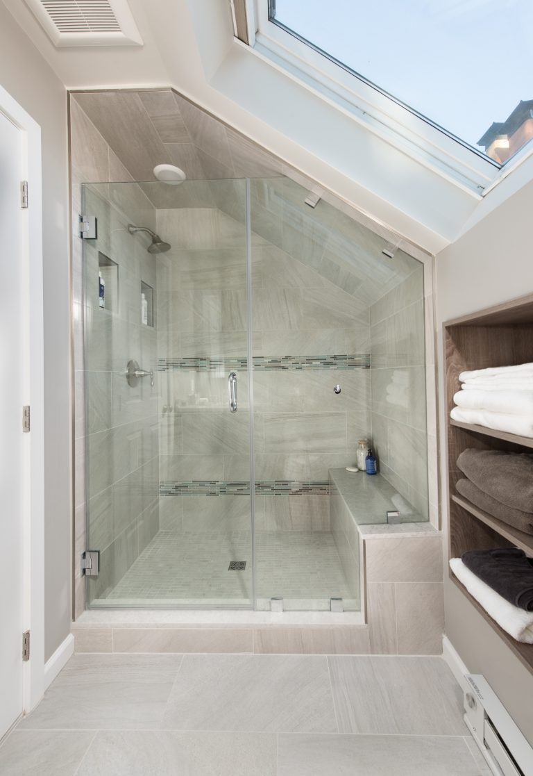large shower with glass wall and built in bench stripe tile features sloped ceiling with skylight