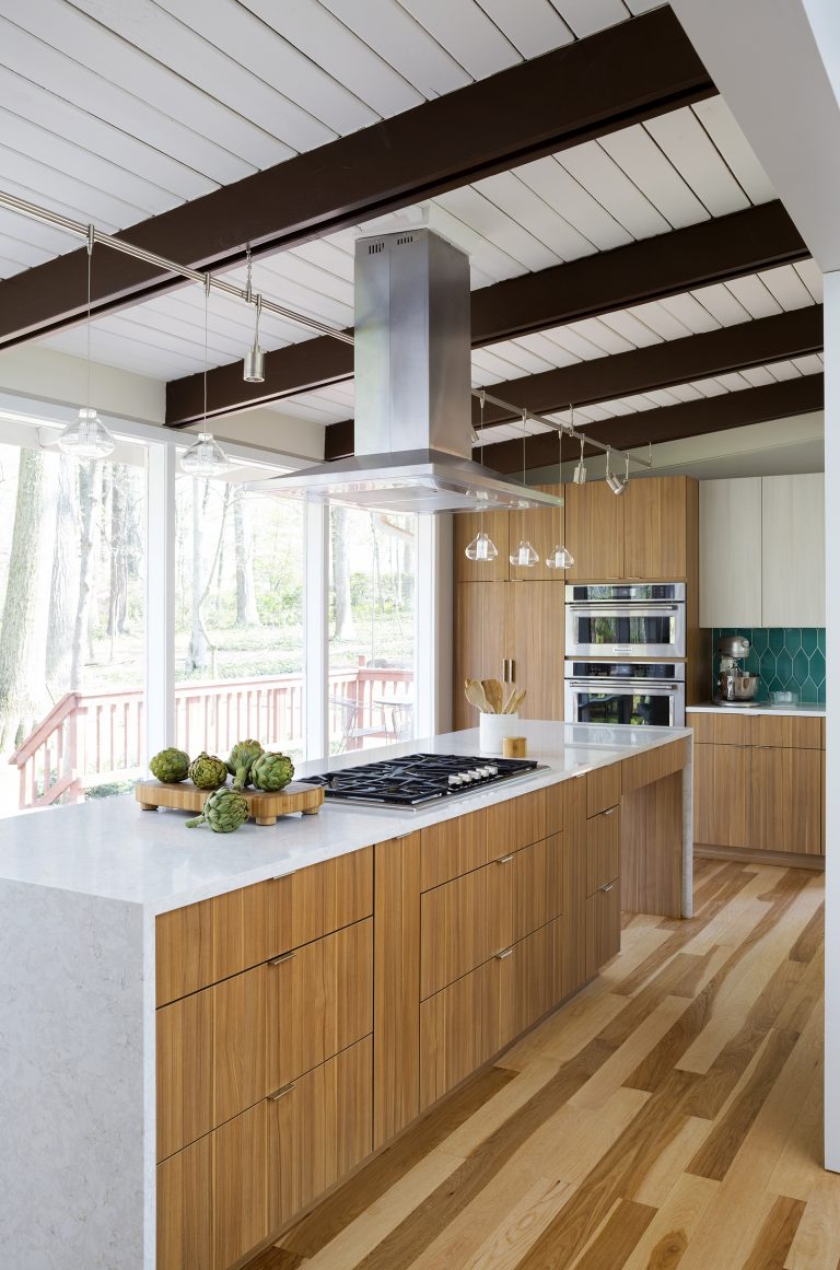 modern kitchen natural wood cabinetry and floors waterfall edge countertops teal tile backsplash beam ceiling