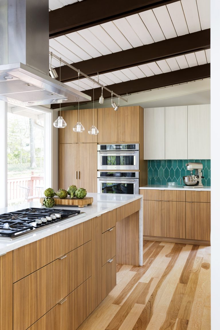 modern kitchen natural wood cabinetry and floors waterfall edge countertops teal tile backsplash beam ceiling