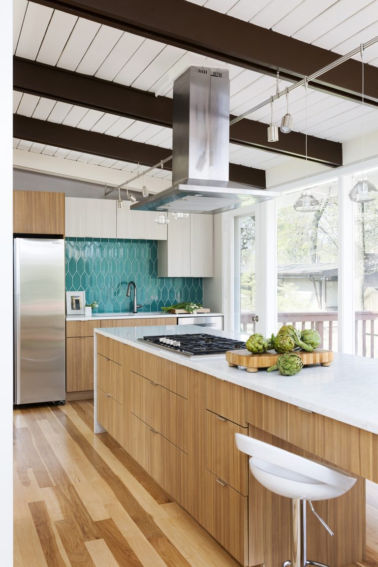 modern kitchen natural wood cabinetry and floors waterfall edge countertops teal tile backsplash beam ceiling