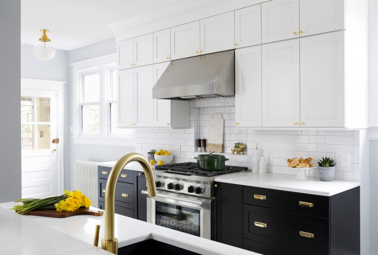 kitchen with black lower cabinetry and white upper cabinetry brushed gold fixtures stainless steel appliances
